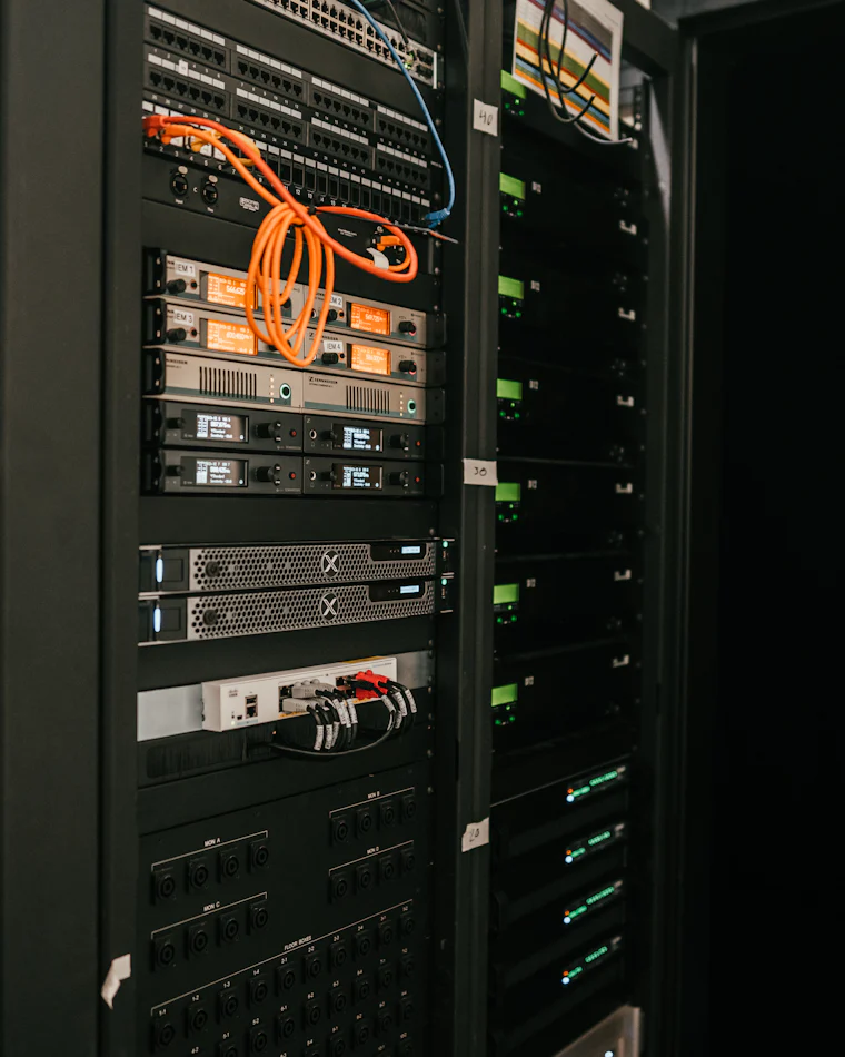Server rack with patch panels, switches and an orange patch cable in a dark equipment room